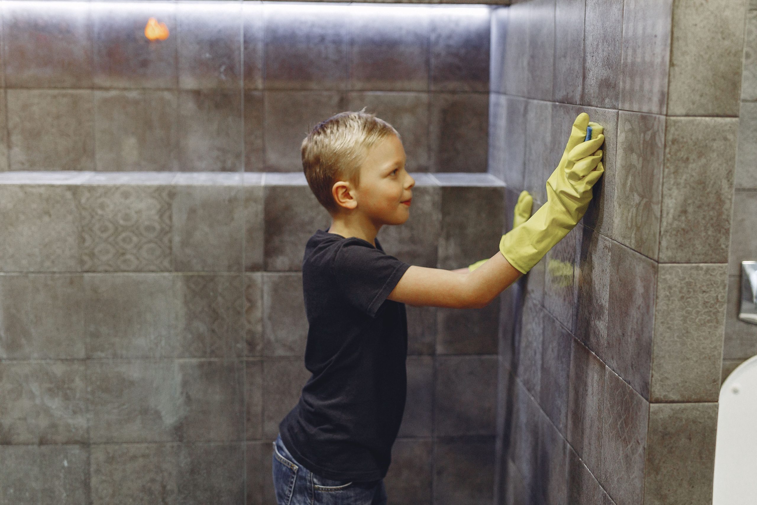 Enfant en gants jaunes nettoyant mur carrelé salle bain